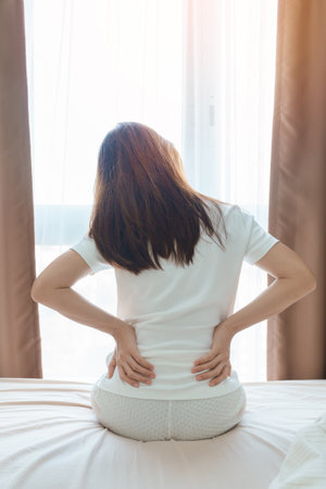 woman having back body ache during sitting on bed at home. adult female with muscle pain after Waking up due to Piriformis Syndrome, Low Back Pain and Spinal Compression. Health medical conceptの写真素材
