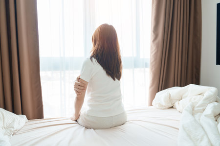 Woman having arm pain during sitting on bed at home, muscle injury and ache after waking up. Health and medical conceptの写真素材