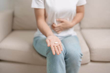 woman hand holding medicine painkiller pill and water glass on the sofa at home, taking for headaches,  stomach ache, Diarrhea Pain from food poisoning, Endometriosis, Hysterectomy and Menstrualの写真素材