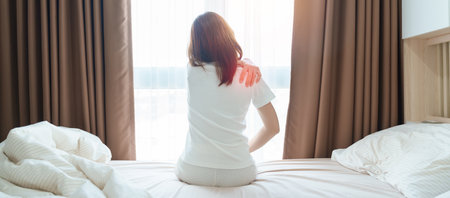 Woman having Shoulder and Neck pain during sitting on bed at home. Muscle painful due to Myofascial pain syndrome and Fibromyalgia, rheumatism, Scapular pain, Cervical Spine. Waking and Health conceptの写真素材
