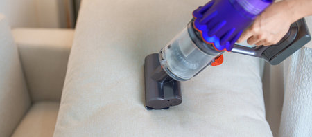 Woman cleaning pillow with cordless Vacuum cleaner. Housewife using wireless Hoover for big cleaning...