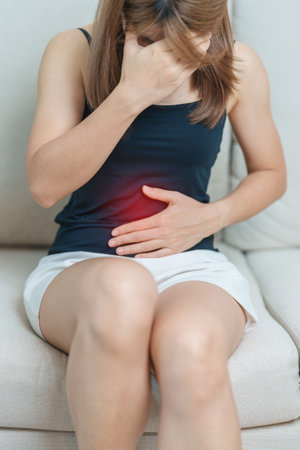 woman having abdomen ache due to Stomach pain, digestion with constipation or Diarrhea from food poisoning, female problem and Endometriosis, Hysterectomy, Stomachache and Menstrual on sofa at homeの写真素材