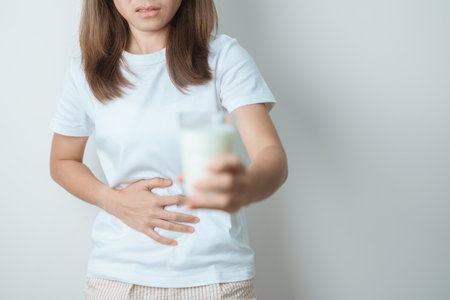 Lactose intolerance and Milk allergy concept. woman hold Milk glass and having abdominal cramps and pain when drink Cow Milk. Symptom stomach ache, Dairy intolerant, Nausea, Bloating, Gas and Diarrheaの写真素材