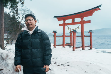man  tourist sightseeing Japanese Torii gate  Shrine and lake Tazawa. Traveler travel in Semboku city, Akita Prefecture, Japan. Landmark for tourist attraction in Tohoku. Japan travel and vacationの写真素材