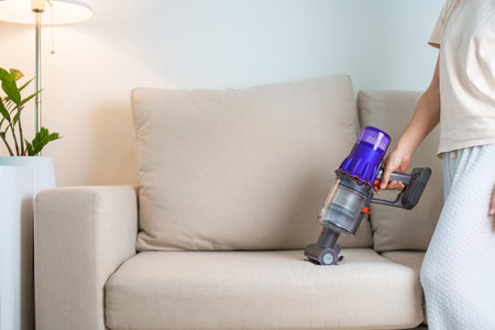 Woman cleaning Sofa with cordless Vacuum cleaner. Housewife using wireless Vacuum for big cleaning home. Housework, Housecleaning, Housekeeping, Removes dust, Domestic hygiene and daily routineの写真素材