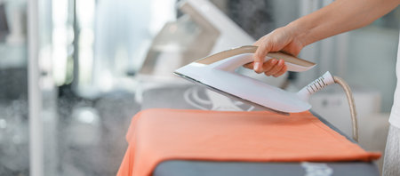Woman hold Electric hot iron press T shirt clothes on ironing board, Intelligent automatic steam iron. Laundry, Housework, Housekeeping, Domestic hygiene, household of chores and daily routine conceptの写真素材