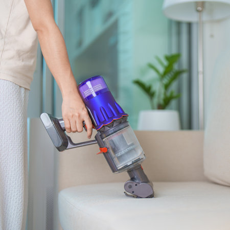 Woman cleaning Sofa with cordless Vacuum cleaner. Housewife using wireless Vacuum for big cleaning home. Housework, Housecleaning, Housekeeping, Removes dust, Domestic hygiene and daily routineの写真素材