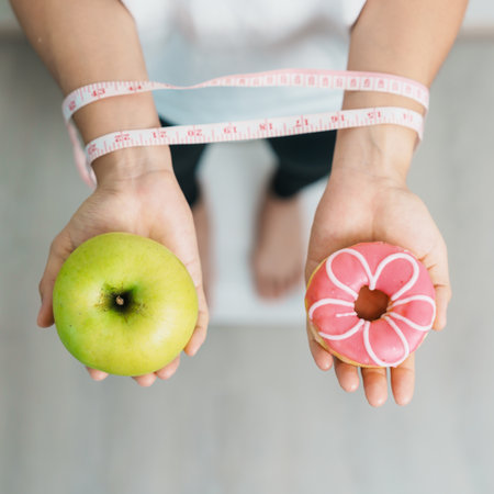woman on weight scale and hand hold green Apple and donut, choose between fruit is Healthy and sweet is Unhealthy junk food. Dieting control, Weight loss, Obesity, eating lifestyle and nutritionの写真素材