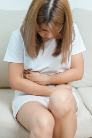 woman having abdomen ache due to Stomach pain, digestion with constipation or Diarrhea from food poisoning, female problem and Endometriosis, Hysterectomy, Stomachache and Menstrual on sofa at homeの写真素材
