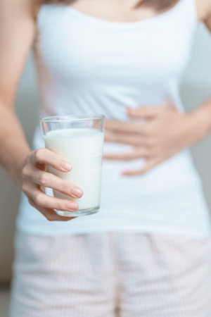 Lactose intolerance and Milk allergy concept. woman hold Milk glass and having abdominal cramps and pain when drink Cow Milk. Symptom stomach ache, Dairy intolerant, Nausea, Bloating, Gas and Diarrheaの写真素材