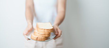 Bread eating and Daily Routine concept. Young woman Hand holding sliced whole grain bread in the morning at homeの写真素材