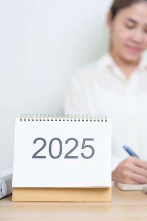 2025 Year Calendar on table with business woman using laptop computer, working and writing in...