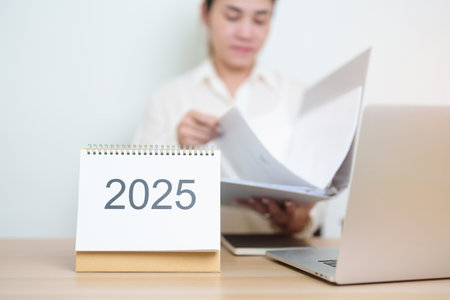 2025 Year Calendar on table with business woman using laptop computer, working and writing in office. countdown, Happy New Year, Resolution, Year End and New Start and Goals Plan Action Conceptの写真素材