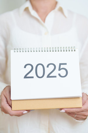 Business woman hand holding and change 2025 Year Calendar on white background table in office. countdown, Happy New Year, Resolution, Year End and New Start and Goals Plan Action Conceptの写真素材
