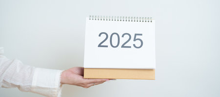 Business woman hand holding and change 2025 Year Calendar on white background table in office. countdown, Happy New Year, Resolution, Year End and New Start and Goals Plan Action Conceptの写真素材