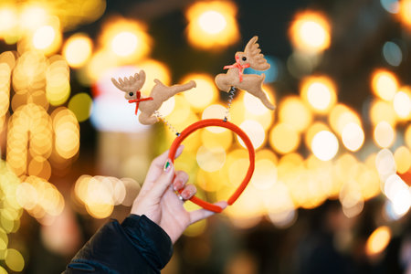Woman hand holding reindeer hat at German christmas market. Merry Christmas, holiday and happy New...