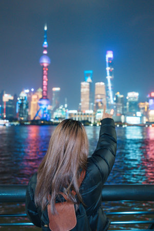 woman traveler visiting in Shanghai, China. Female Tourist with backpack sightseeing Shanghai view of Lujiazui in The Bund of Shanghai at night. landmark and popular for tourism attractionsの写真素材