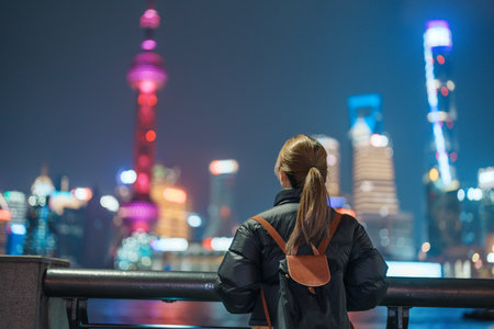 woman traveler visiting in Shanghai, China. Female Tourist with backpack sightseeing Shanghai view of Lujiazui in The Bund of Shanghai at night. landmark and popular for tourism attractionsの写真素材