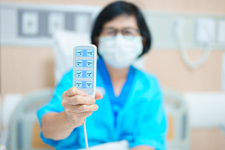 Elderly asian Woman patient hand using remote control for adjust level bed in hospital room. Happy Senior illness resting on comfortable electric bed in modern hospitalの写真素材