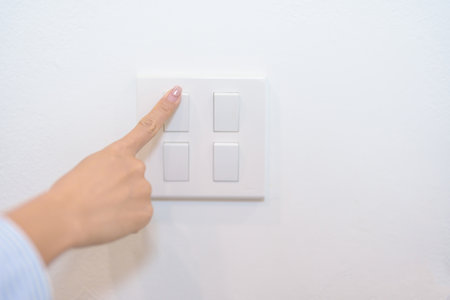 Female finger pushing for turn on light switch on white wall at home room. Woman hand turn off...