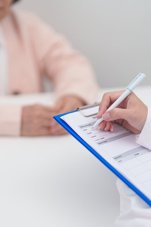 senior woman consulting with doctor in hospital. Elderly patient talking and sharing disease. Doctor listens, asking question and taking note. medical consultation and geriatric Healthcare conceptの写真素材