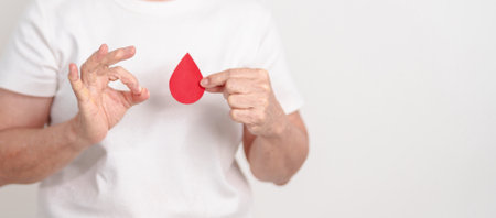 Elderly woman with red Blood drop paper for concept of June World Blood Donor day, Donation, April Hemophilia awareness day, May Thalassemia Day, Anemia awareness, June Sickle Cell and Blood Disordersの写真素材