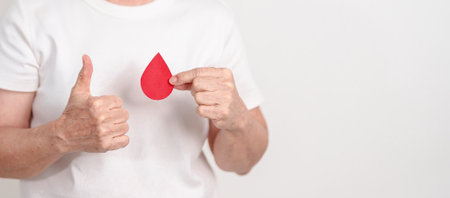 Elderly woman with red Blood drop paper for concept of June World Blood Donor day, Donation, April Hemophilia awareness day, May Thalassemia Day, Anemia awareness, June Sickle Cell and Blood Disordersの写真素材