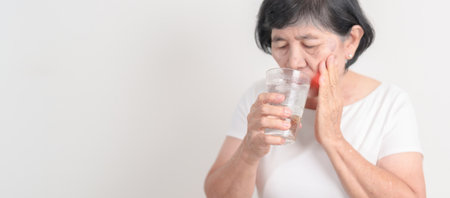 Elderly woman having toothache and pain after drink ice water for concept of Teeth Sensitive to Cold, Tooth Decay and Gum Disease, Grinding Teeth and Stress, Exposed Nerve Roots, Crack and Recedingの写真素材