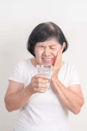 Elderly woman having toothache and pain after drink ice water for concept of Teeth Sensitive to Cold, Tooth Decay and Gum Disease, Grinding Teeth and Stress, Exposed Nerve Roots, Crack and Recedingの写真素材