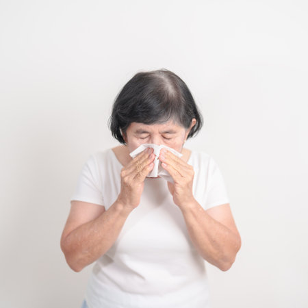 Elderly woman blowing her nose with tissue for concepts of Common Cold, Influenza, Flu, Hay, Fever, Covid 19, Respiratory Infection, Sinusitis, Allergic Rhinitis, Allergy, Medical and health careの写真素材