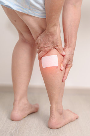 Elderly woman having Calf pain with Medicated pain relief patch plaster for concepts of Calf Muscle Strain, muscle pull, Leg Cramp, Sprain, aches, Varicose Veins, Deep Vein and world Thrombosis dayの写真素材