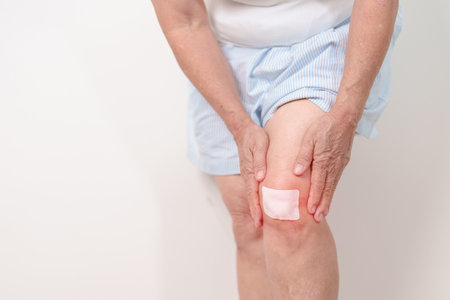 Elderly woman having knee ache with Medicated pain relief patch plaster to Runners Knee or Patellofemoral Pain Syndrome, osteoarthritis, arthritis, rheumatism and Patellar Tendinitis. Senior healthの写真素材