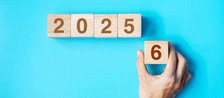 hand holding wooden cube block with 2026 text on blue background. Resolution, plan, review, goal,...