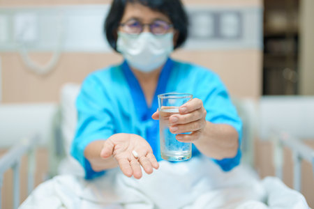 Elderly asian Patient Woman hold pill and glass of fresh water. Female Senior take medicine tablets in hospital. Influenza, Fever, illness, treatment, Insurance, Healthcare, medical and Medicine dayの写真素材
