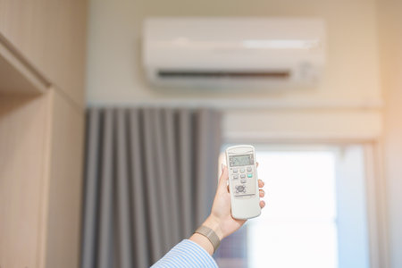 operating and adjusting Air conditioner temperature by remote control in home. Hand holding remote control and setting comfortable temperature on climate system in office or apartment. hot and coolの写真素材