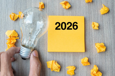 2026 Idea words on yellow note and crumbled paper with Businessman holding lightbulb on wooden table background. New Year New Start Creative, Innovation, Imagination, Resolution and Goal conceptの写真素材