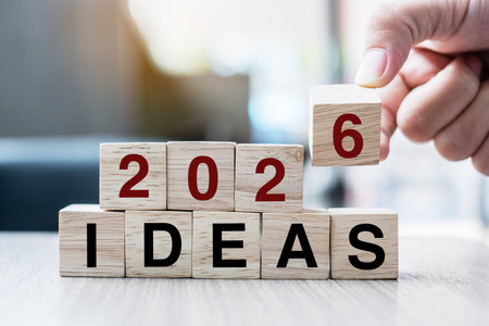 Businessman hand holding wooden cube with flip over block 2025 to 2026 Plans word on table background. Resolution, strategy, solution, goal, business and New Year holiday conceptsの写真素材