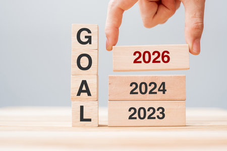 hand pulling 2024 block over 2025 and 2026 wooden building on table background. Business planning,...