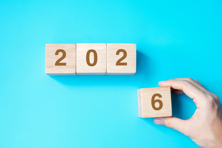 hand holding wooden cube block with 2026 text on blue background. Resolution, plan, review, goal,...