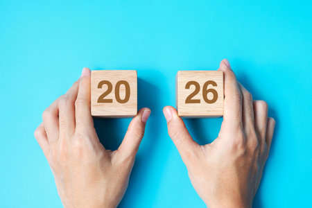 hand holding wooden cube block with 2026 text on blue background. Resolution, plan, review, goal,...