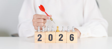 Hand holding red dart over people chess and 2026 year blocks. Goal, plan, action, target, strategy,...