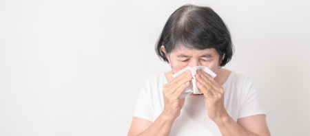 Elderly woman blowing her nose with tissue for concepts of Common Cold, Influenza, Flu, Hay, Fever,...