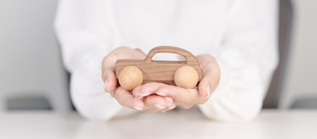 Woman hand holding wood car toy. Car insurance, warranty, rental, Financial, new and repair conceptの写真素材