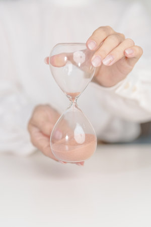 Woman with Hourglass on table office, Sand flowing through the bulb of Sandglass measuring the passing time.の写真素材
