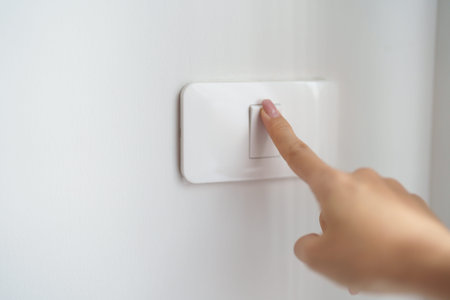Female finger pushing for turn on light switch on white wall at home room. Woman hand turn off...