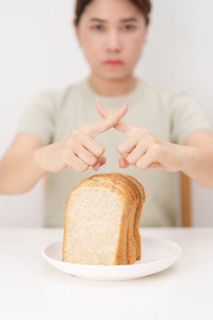 Unhappy woman showing Rejecting gesture and refusing to eat bread. concept of gluten intolerance, gluten sensitivity, carb loading concerns, or a disliking for unhealthy dietary habitsの写真素材