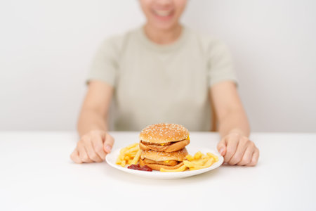 happy woman eating Juicy beef burger with melted cheddar cheese, potato chips. Unhealthy, High calorie, Fast food craving, Obesity, diet, weight loss, junk food and lifestyleの写真素材
