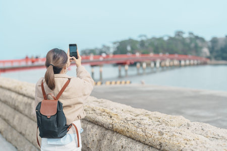Woman tourist taking photo Fukuura jima bridge or the bridge of romantic encounters for Fukuura...