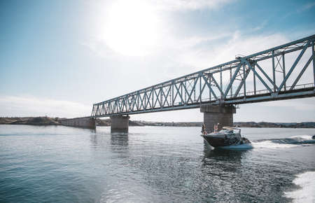 Boat floats on water under bridge on clear summer day.