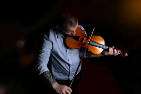 A man in a blue shirt plays the violin on a black background.